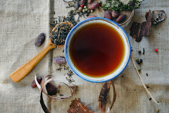 Bols de fleurs et de fruits séchés destinés à l'infusion, disposés autour d'une tasse fumante